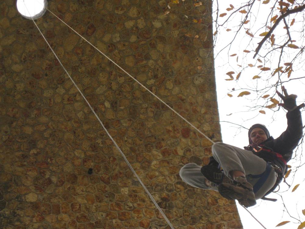 Jonathan en descente de rappel sous une arche de pierre, harnais et corde d'escalade