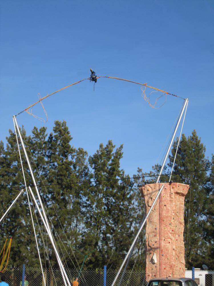 Un pratiquant propulsé en pleine hauteur sur le bungy trampoline, avec le mur d'escalade en arrière-plan